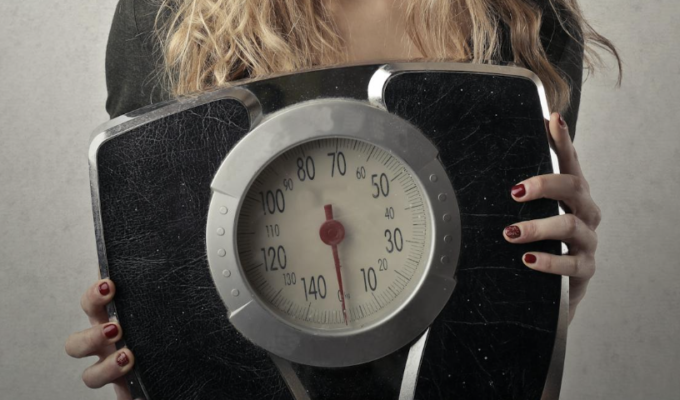 Persoon die op een weegschaal staat met een glimlach op het gezicht als symbool voor gezond gewichtsverlies zonder dieet.