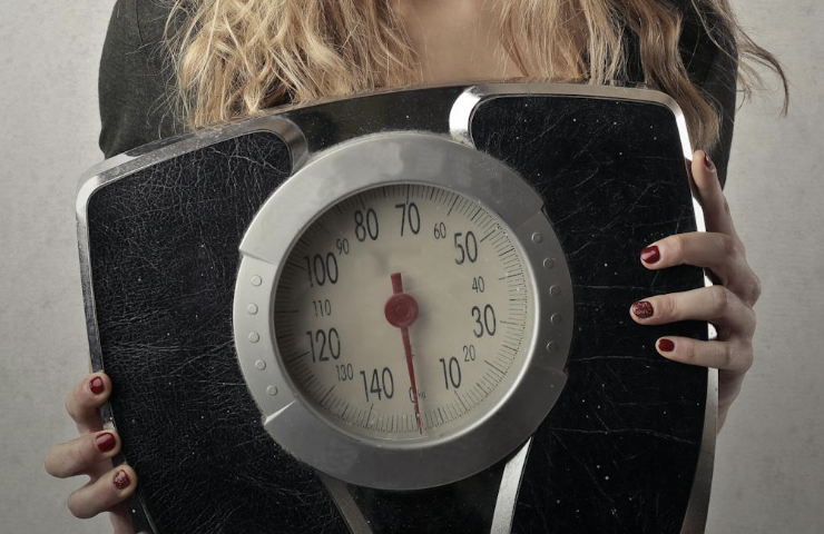 Persoon die op een weegschaal staat met een glimlach op het gezicht als symbool voor gezond gewichtsverlies zonder dieet.
