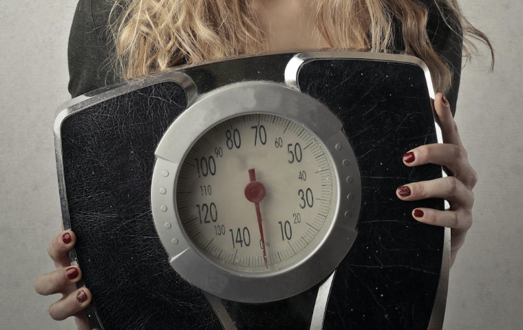 Persoon die op een weegschaal staat met een glimlach op het gezicht als symbool voor gezond gewichtsverlies zonder dieet.