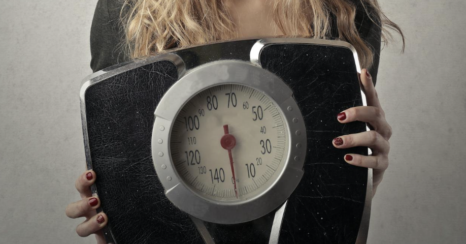 Persoon die op een weegschaal staat met een glimlach op het gezicht als symbool voor gezond gewichtsverlies zonder dieet.